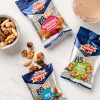 su un tavolo confezioni bbfit ventura mandorle sgusciate noci sgusciate mix frutta secca sgusciata accanto a bicchiere rotondo con frullato e ciotola in ceramica con frutta secca sgusciata mista