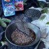 sopra un tavolo nero con tovaglia bianca antica, piatto nero con lenticchie nere cotte, accanto a cucchiaio antico pesante, confezioni chiuse di mirtilli e cranberry ventura e una ciotola nera di lenticchie nere crude