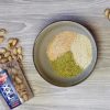 pistacchi in guscio in barattolo rovesciati su un tavolo accanto a ciotola con farina di pistacchi e altri cereali per panatura