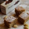 cubetti di torta accanto a scatola di datteri medjoul ventura e mandorle sgusciate e pelate
