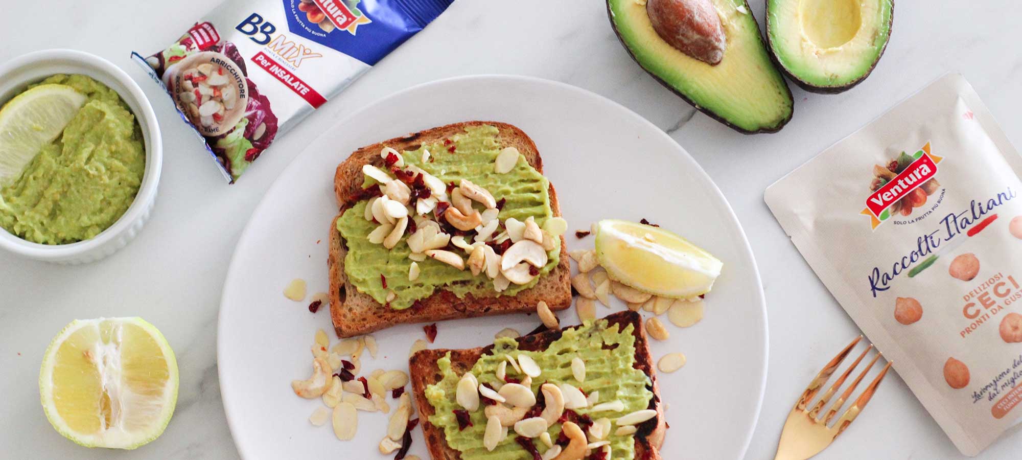 avocado toast fette di pane hummus avocado a meta piatto bianco fette di pane bbmix frutta secca pack rosso fettina limone