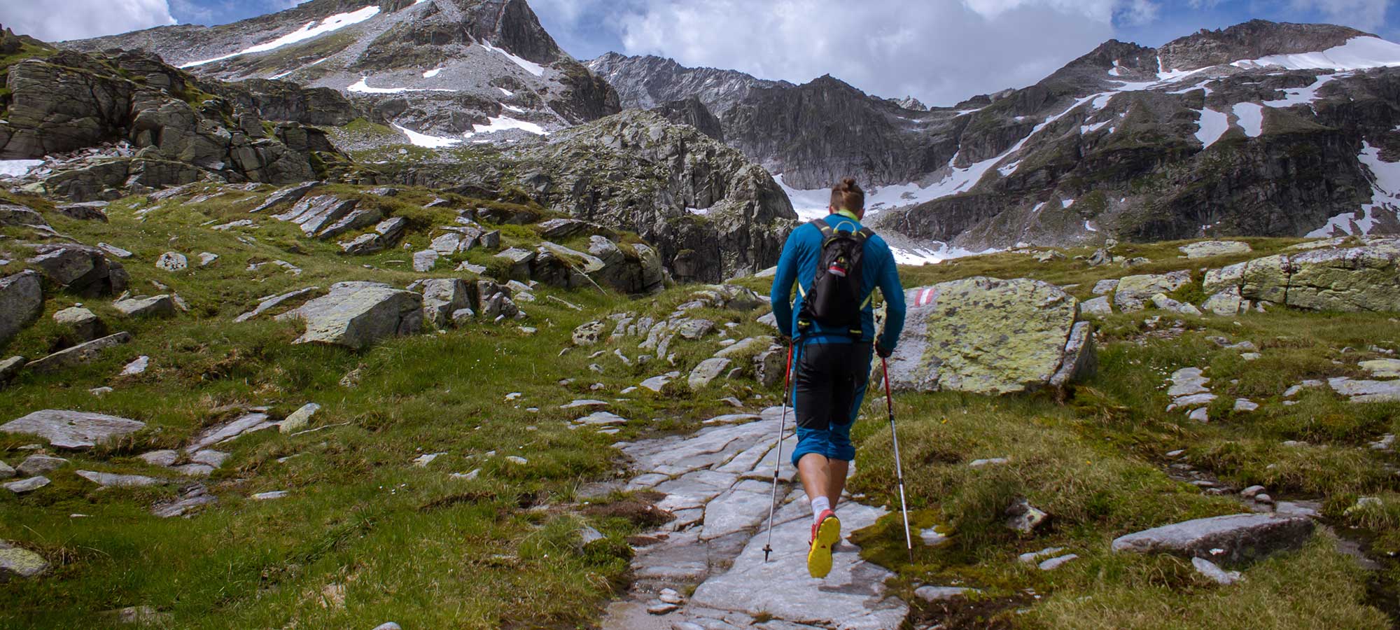 nordic walking uomo con bastoncini e zainetto sentiero di montagna cime pietra ghiaccio erba
