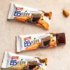 barrette bbextra mandorla e nocciola ventura ricoperte al cioccolato, confezioni aperte e chiuse su tavolo, accanto a una mandorla sgusciata