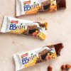 barrette bbextra mandorla e nocciola ventura ricoperte al cioccolato, confezioni aperte e chiuse su tavolo, accanto a nocciole sgusciate