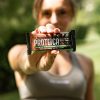 donna vestita sportiva al parco con belle unghie curate tiene in mano barretta proteica ventura con frutta secca e cioccolato