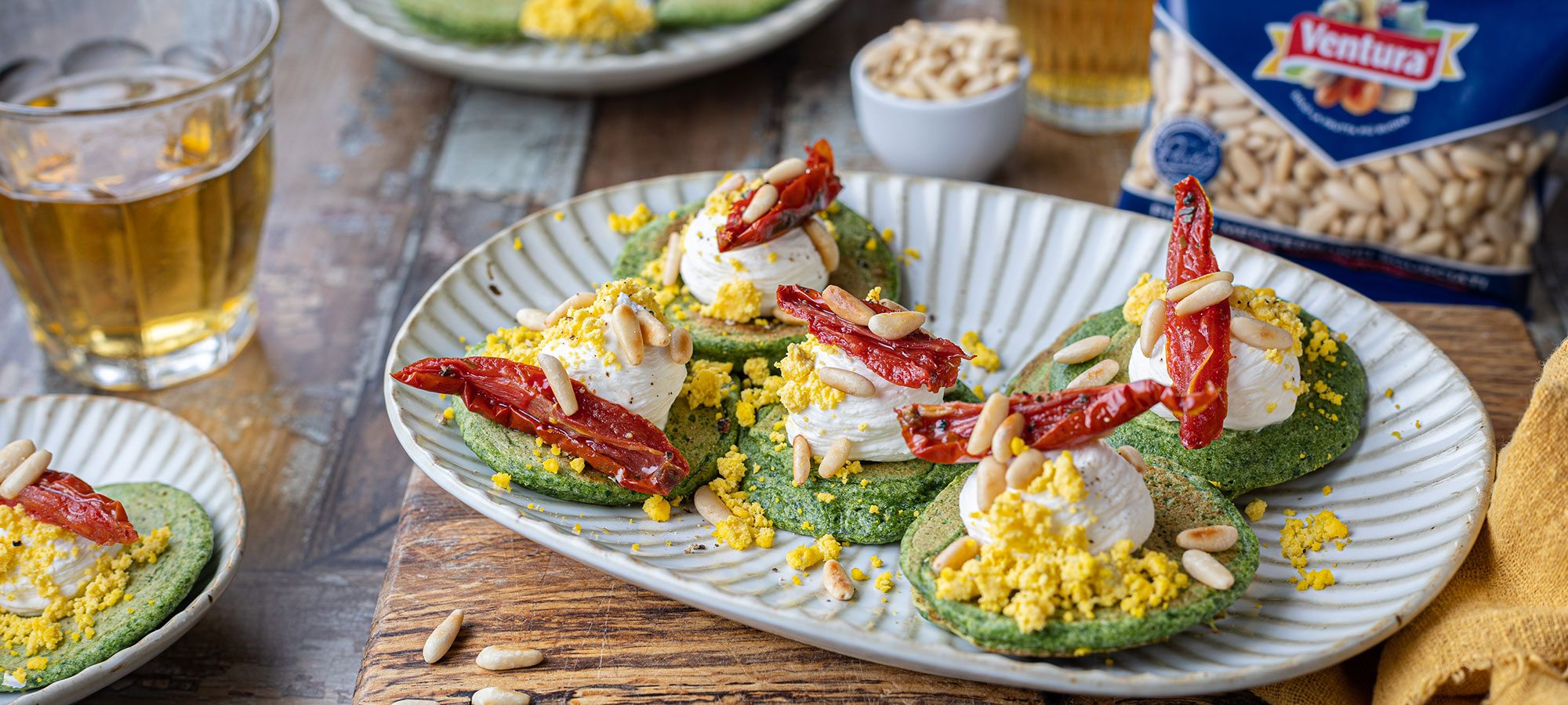 antipasto facile blinis di spinaci crespelle con pomodori sott olio mimosa tuorlo d uovo sbriciolato pinoli ventura in un piatto bianco su tagliere di legno