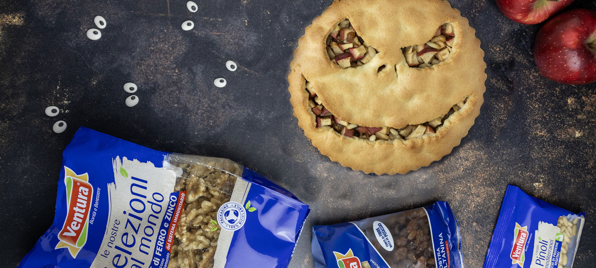 crostata strudel ispirata a nightmare before christmas su tavolo in pietra nera con busta noci sgusciate uvetta pinoli e occhietti adesivi