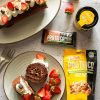 su un tavolo, rotolo al cacao con panna e fragole, pack frutta secca proteico ventura, barretta proteica al cioccolato e barattolo con adesivo giallo