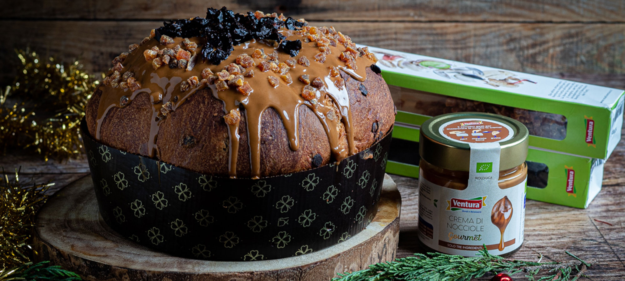 panettone decorato con crema di nocciole e frutta essiccata su tronco di legno accanto a barattolo crema e blister frutta secca my nut