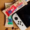barretta bbmix ricarica ventura incartata accanto ad altre barrette a base di frutta secca e a un videogame portatile spento